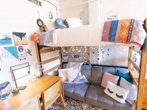 Interior of a dorm room with a sofa below loft bed, light strings and colorful throws and pillows